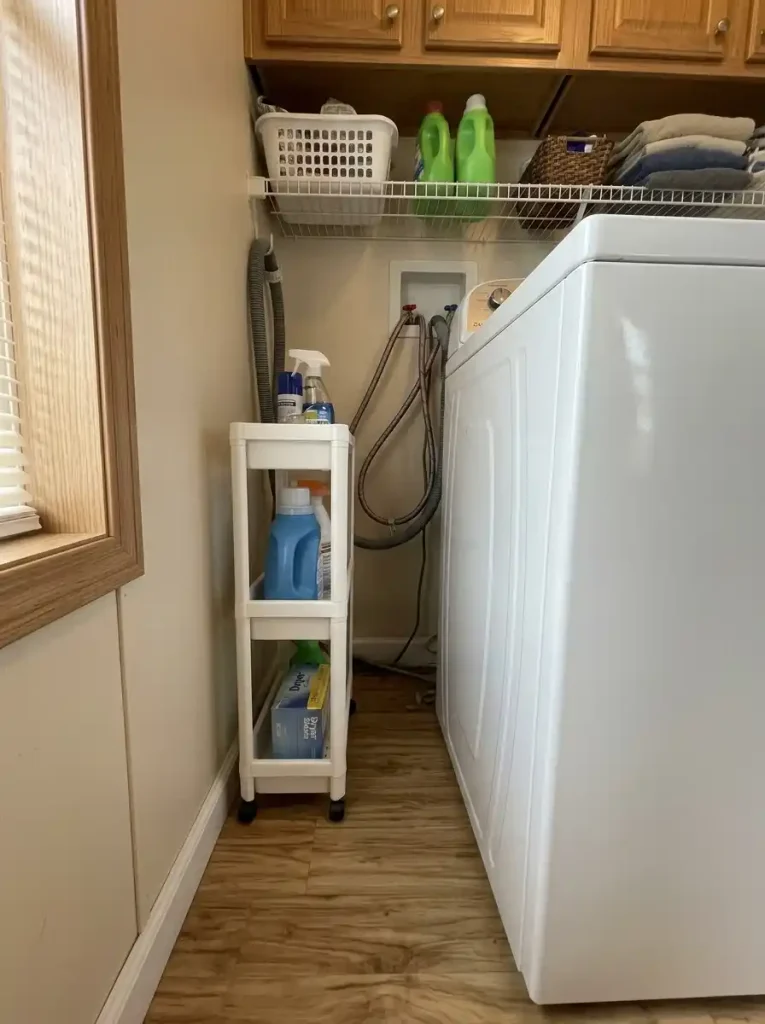 Narrow rolling laundry storage beside a washer with the appliance access area still visible and reachable.