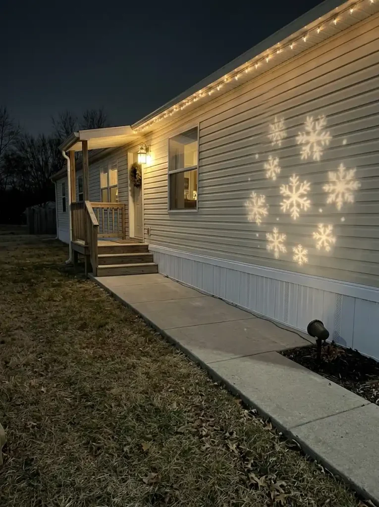 Soft white snowflake projections on a plain section of mobile-home siding at night, away from windows and the clear front walkway.