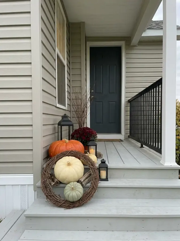 Tall flowers, branches and layered pumpkins fill one deep corner while most of a tiny mobile-home porch remains open.