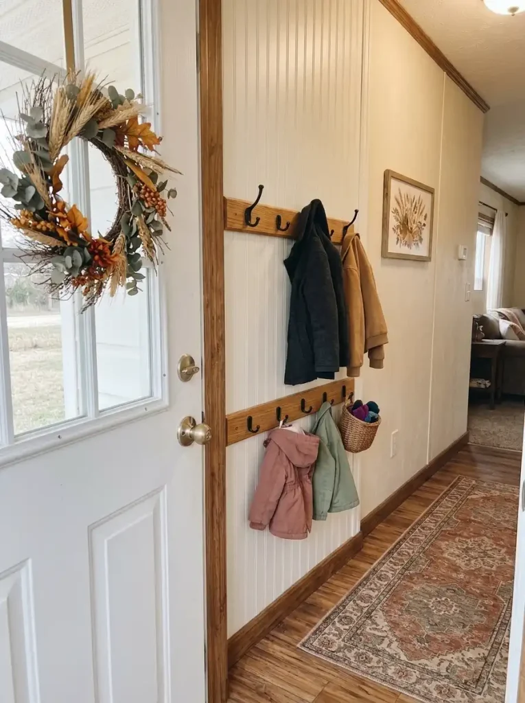 Two rows of coat hooks with adult jackets above shorter children's jackets on a small mobile home entry wall.