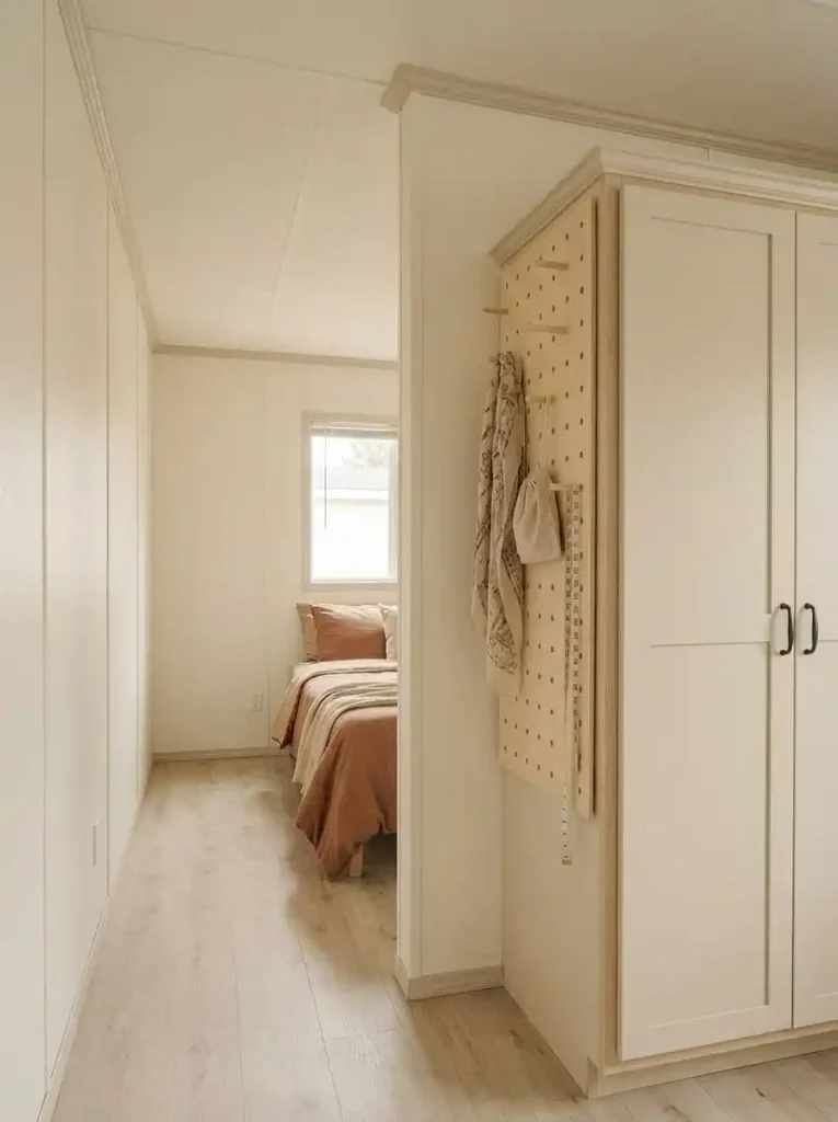 Shallow pegboard on the exposed side of a wardrobe in a small mobile home bedroom with the adjacent walking path left clear.