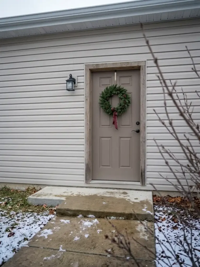 Compact pinecone-and-evergreen Christmas decoration on an exposed manufactured-home front door.