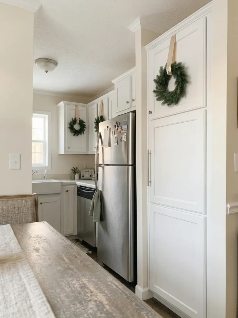 White Shaker kitchen cabinets with small Christmas wreaths suspended from soft champagne satin ribbons.