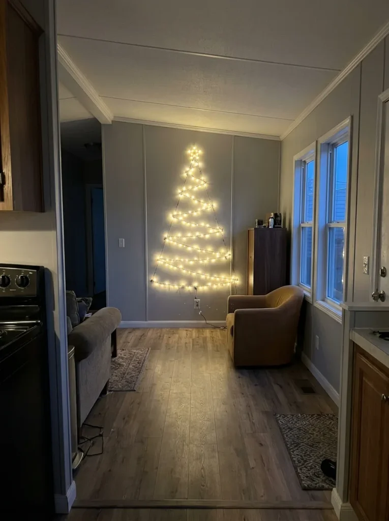 Warm-white zigzag Christmas lights forming a flat tree on the end wall of a narrow single-wide mobile home.
